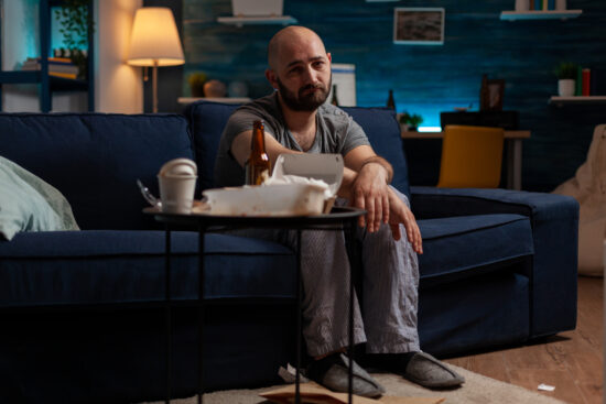 Disappointed poor man with chronic depression sitting on sofa